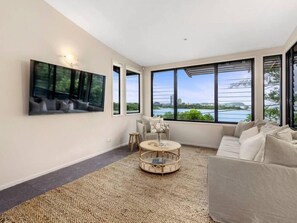 A modern living room with a large window, a sofa, a coffee table, and a painting on the wall. - Currumbin Beachfront Haven (Currumbin)