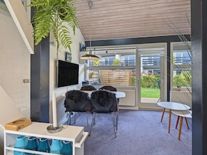 Een moderne woonruimte met een flatscreen televisie, een eethoek met stoelen, een klein tafeltje en een groot raam met uitzicht op de omgeving.