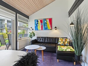 Een moderne woonkamer met een zwarte leren bank, twee witte ronde tafels en kleurrijke abstracte schilderijen aan de muur.
