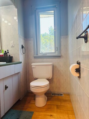 A bathroom with a toilet, a window, a sink, and a shower.