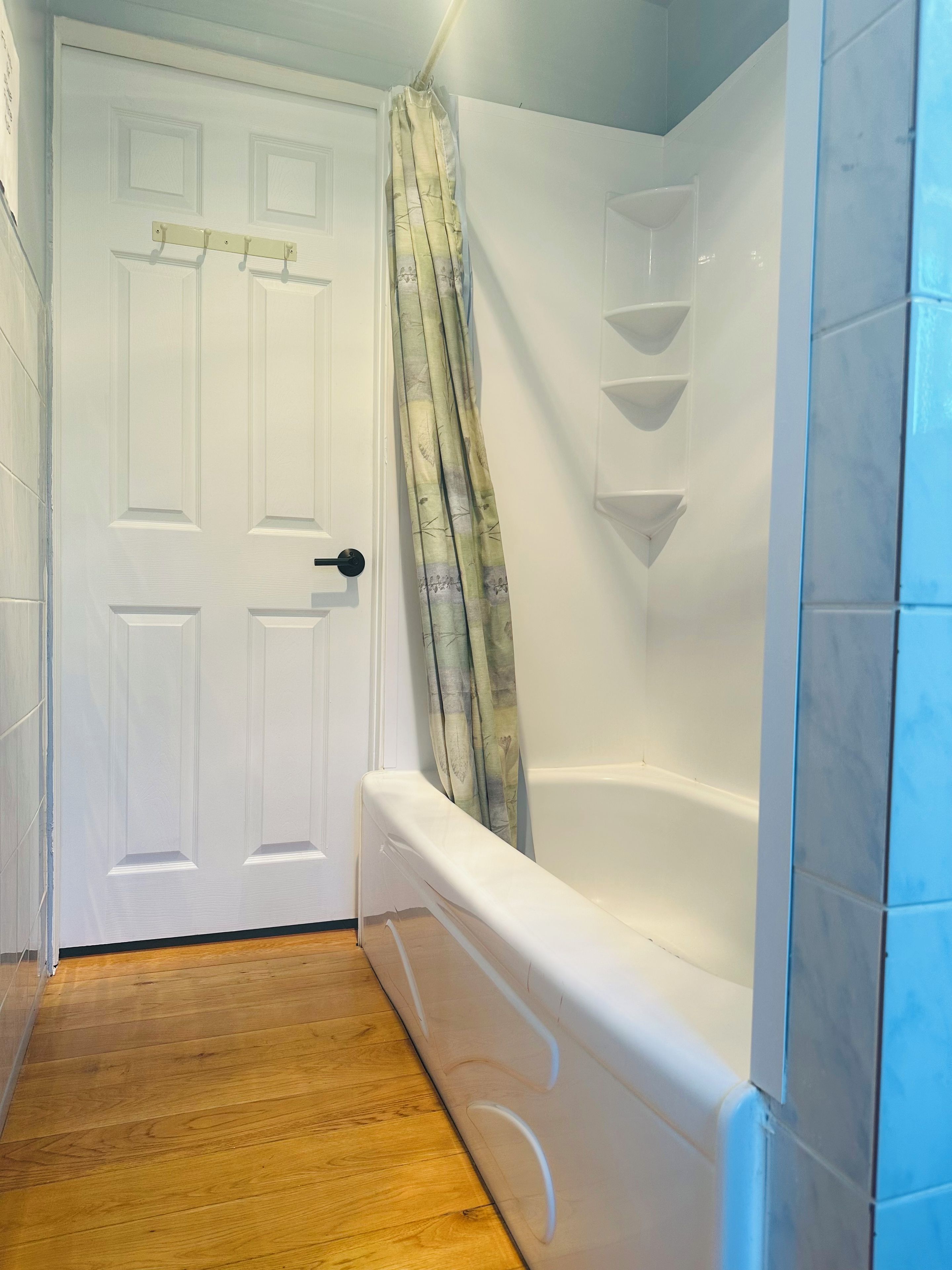 A bathroom with a white door, a bathtub, and a shower area.