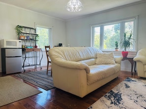 A living room with a beige sofa, a dining area with a wooden table, a refrigerator, and a potted plant.