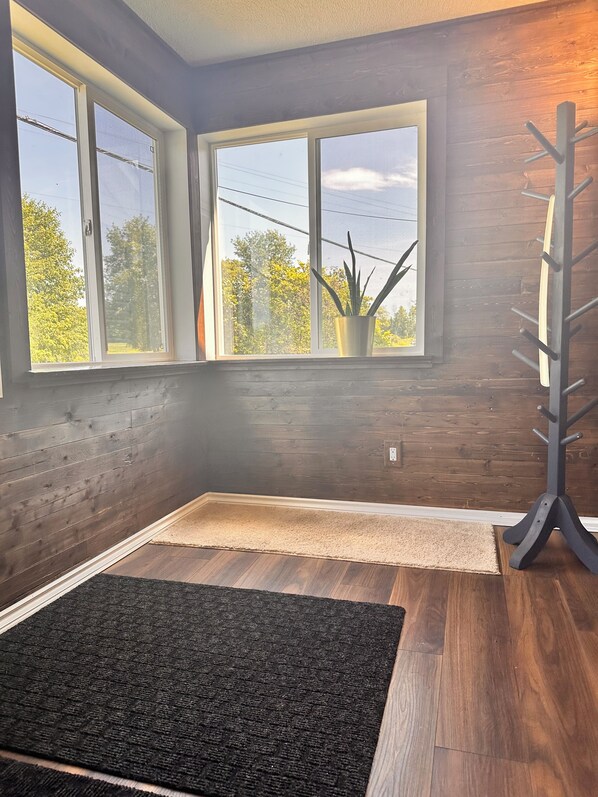 A room with wooden walls, a large window, a black rug, and a coat rack.