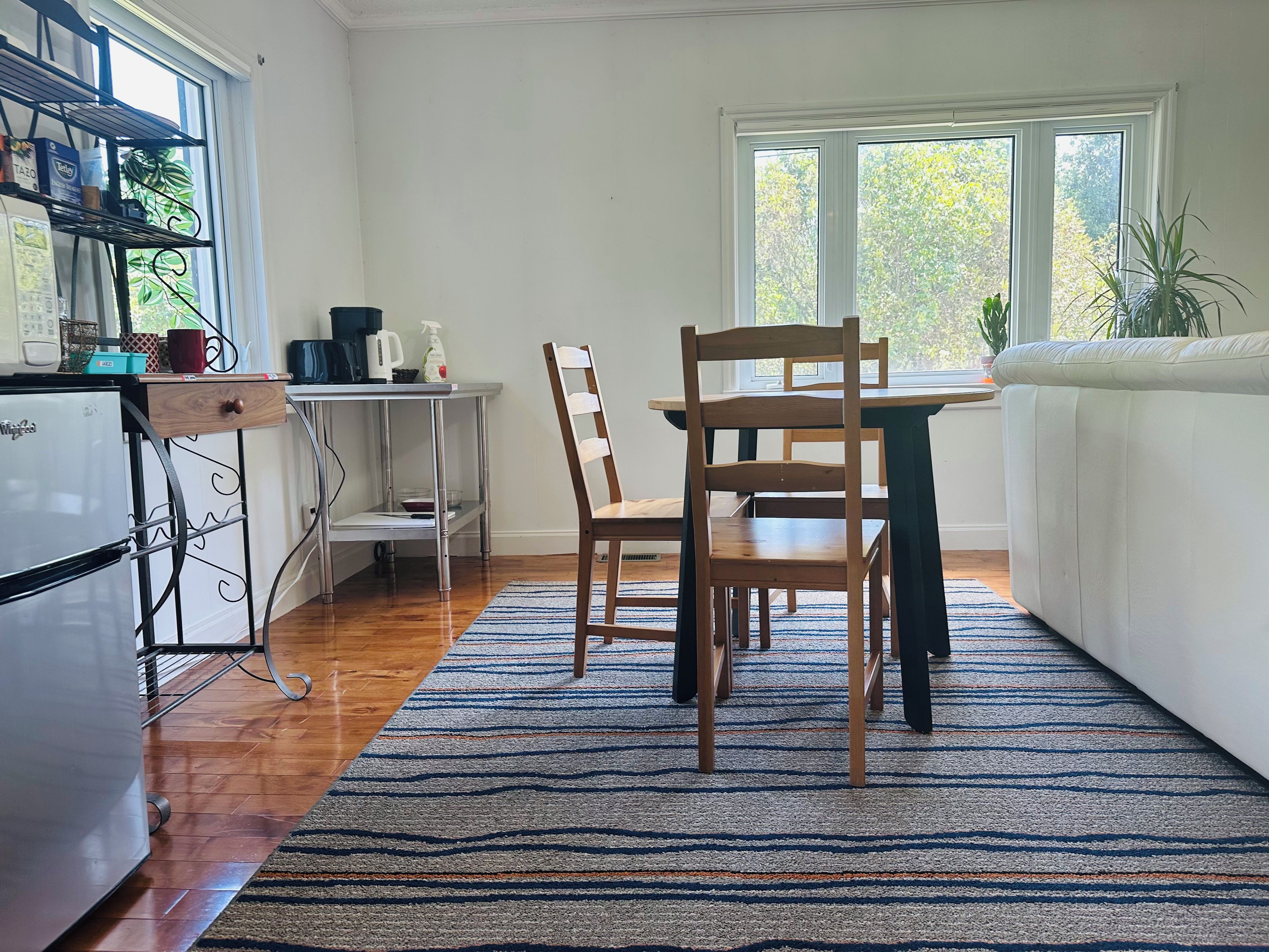 Une cuisine compacte comprenant un réfrigérateur, une table à manger en bois et des chaises. Une fenêtre laisse entrer la lumière naturelle et offre une vue sur la verdure environnante.