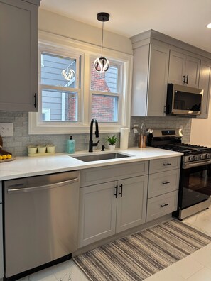 A modern kitchen with grey cabinetry, a stainless steel dishwasher, a black stove, and a microwave above the counter. - 4-bedroom Eastside single home with cool AC for relaxing stay (Providence)
