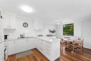 A modern kitchen with white cabinetry, a built-in oven, and a dining area with a wooden table and chairs. - Sanctuary Court 4 Retreat in Currumbin Beach (Currumbin)