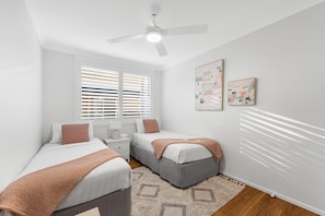 Une chambre avec deux lits, un ventilateur de plafond et deux fenêtres équipées de stores.