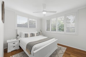 Een slaapkamer met een bed, nachtkastjes, een lamp en een plafondventilator.