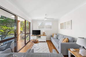 A modern living room with a large sliding glass door leading to a balcony, a flat-screen TV, a sofa, and a coffee table. - Sanctuary Court 4 Retreat in Currumbin Beach (Currumbin)
