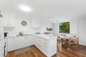 Een moderne keuken met witte kasten, een inbouwoven en een eethoek met houten stoelen en een tafel.