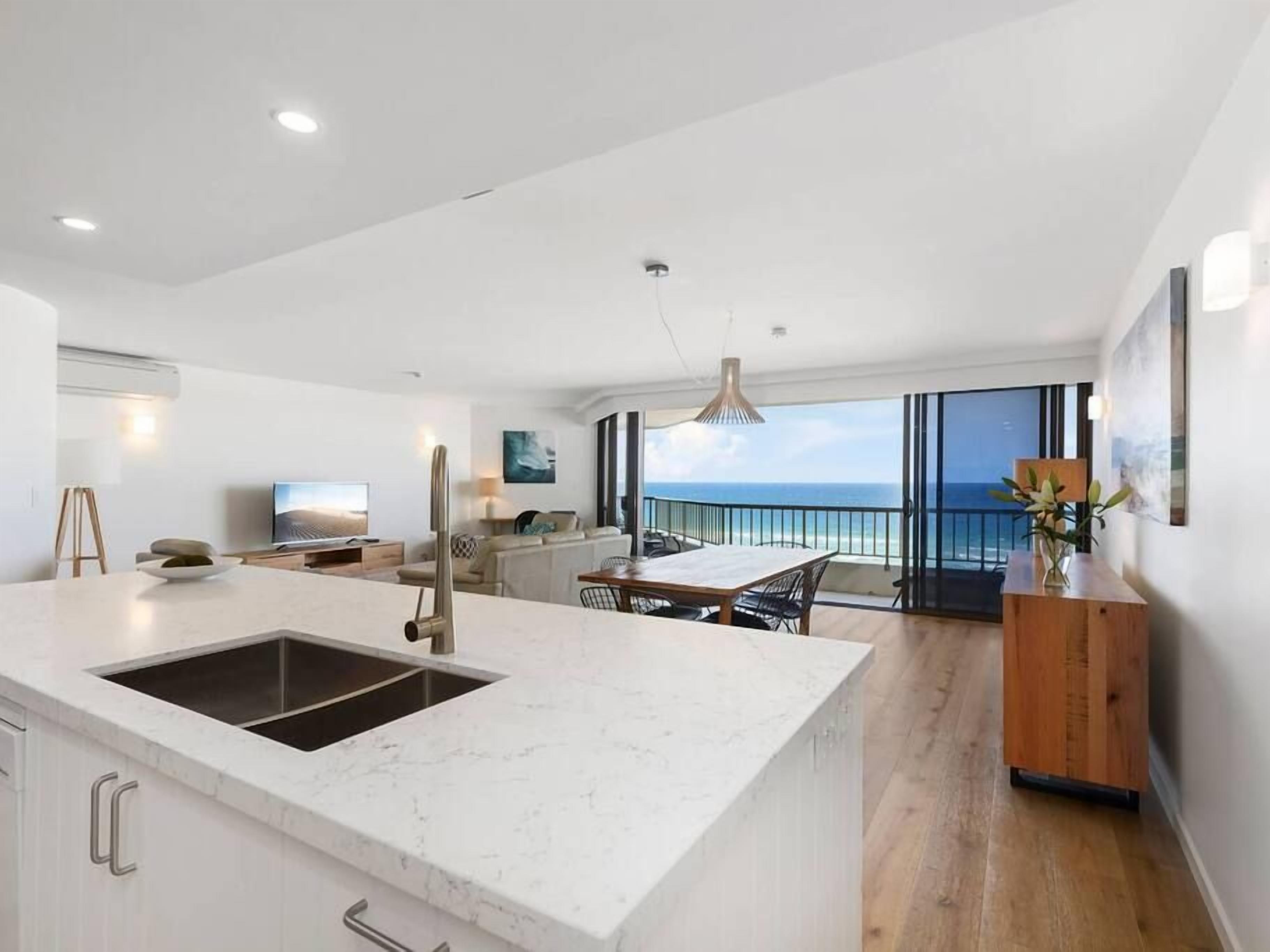 Een moderne keuken met een groot eiland, een eethoek met uitzicht en een houten servieskast.
