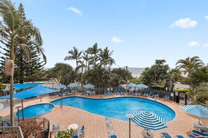 A swimming pool with lounge chairs and umbrellas, surrounded by palm trees. - The Retreat 8G at The Rocks Resort (Currumbin)