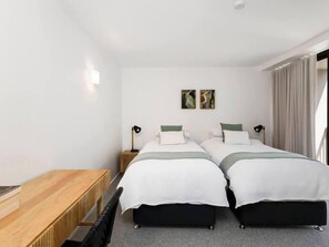 Habitació d'hotel amb dos llits, un escriptori de fusta i una petita taula de nit amb una làmpada.