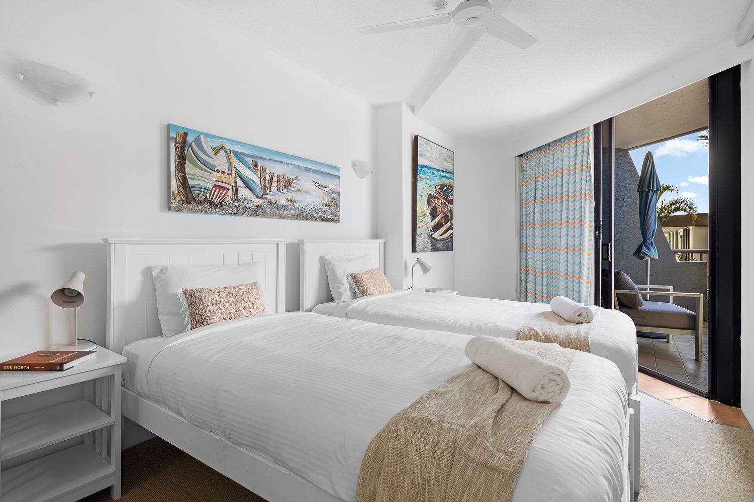 Een hotelkamer met twee bedden, een plafondventilator, kunstwerken aan de wanden en uitzicht op de omgeving.