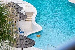 Une piscine à bord incurvé, un poste de surveillance pour les sauveteurs et un parasol en chaume.