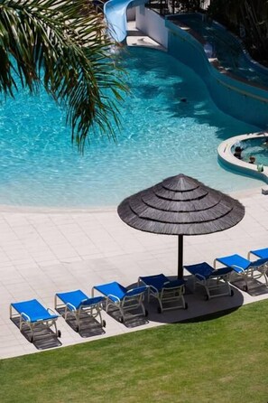 A pool area with a water slide, lounge chairs, and a shaded umbrella. - Ocean Breeze at Palm Beach (Palm Beach)