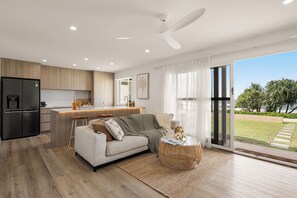 A modern kitchen with a built-in LG refrigerator, a dining area with a bar stool, and a living room with a sofa and a coffee table. - Little Waves Tugun Beach Retreat (Tugun)