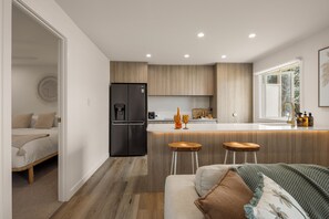 A modern kitchen with a built-in refrigerator, wooden cabinets, and a bar area with stools. - Little Waves Tugun Beach Retreat (Tugun)