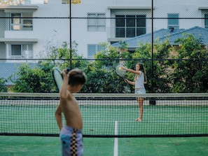 An outdoor tennis court with a net in the middle, surrounded by greenery and buildings in the background. - The Rocks 11H Currumbin Escape with Ocean Views (Currumbin)