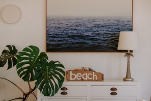 Eine Wand mit einem gerahmten Bild des Meeres, einem Holzschild mit dem Wort 'beach', einer Lampe und einer Pflanze.
