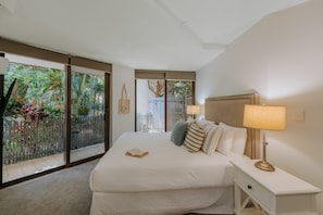 A hotel room with a large bed, a nightstand, a lamp, and a view of a garden through a sliding door. - The Rocks Resort GI Currumbin Escape (Currumbin)
