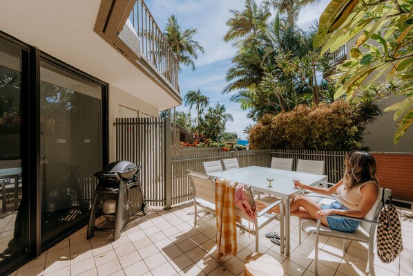 A patio with a table and chairs, a grill, and a view of palm trees and a fence. - The Rocks Resort GI Currumbin Escape (Currumbin)