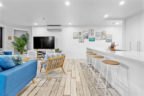 A modern living room with a sofa, a TV, and a bar area with stools. - The Rocks Resort GA  Currumbin Beach apartment (Currumbin)