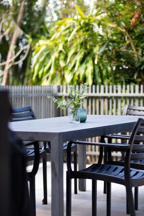 An outdoor patio with a table and chairs, a vase with flowers, and a wooden fence in the background. - The Rocks Resort GA  Currumbin Beach apartment (Currumbin)