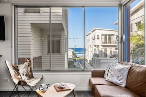 A modern living room with a large sliding glass door, a brown leather sofa, a wooden coffee table, and a unique chair. - Daybreak Loft at Currumbin Beach with Views (Currumbin)