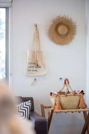 A room with a wicker basket on a stand, a straw hat on the wall, and a tote bag with a message. - Daybreak Loft at Currumbin Beach with Views (Currumbin)