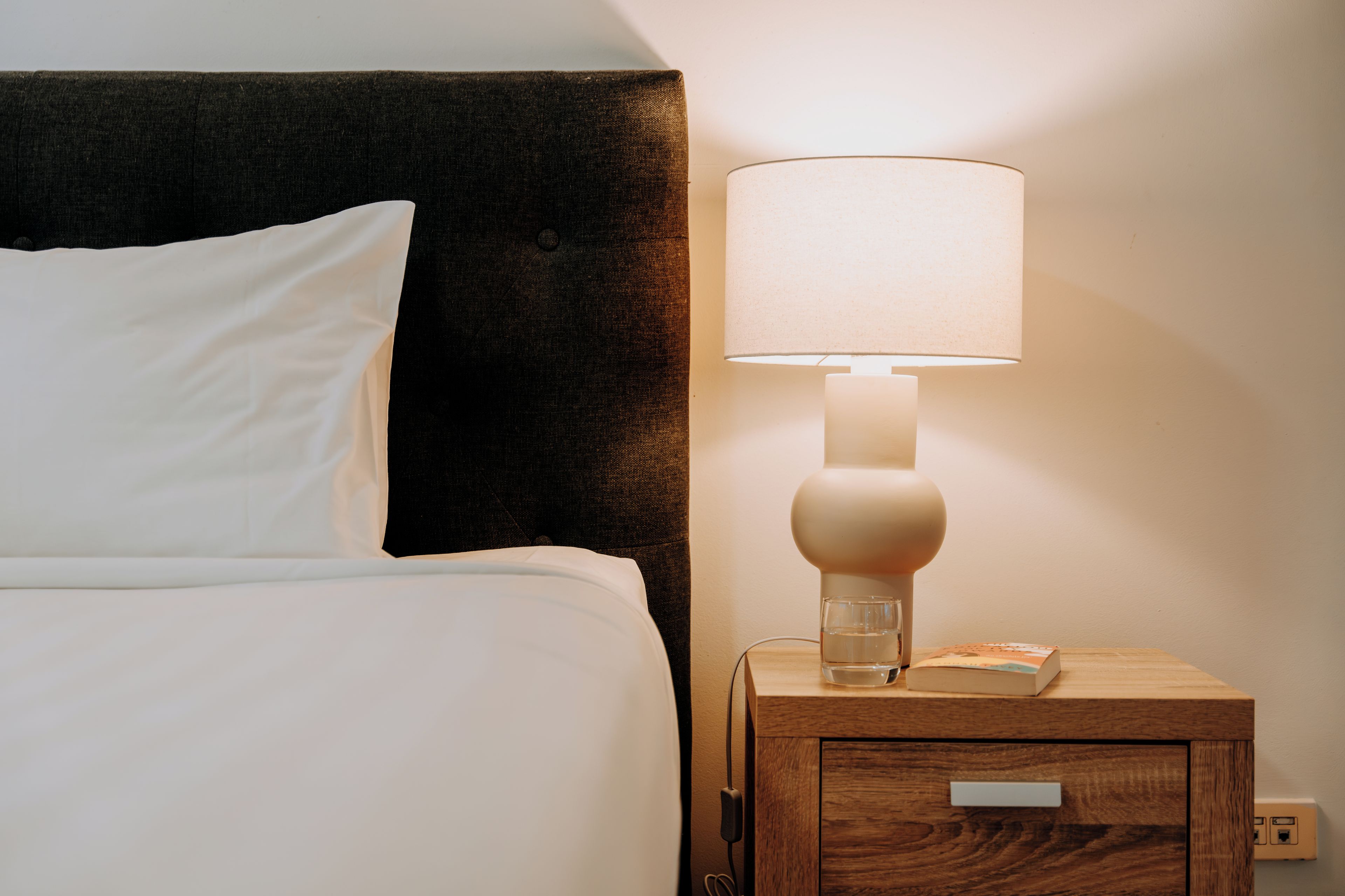 A bed with white bedding, a nightstand with a lamp, and a book.