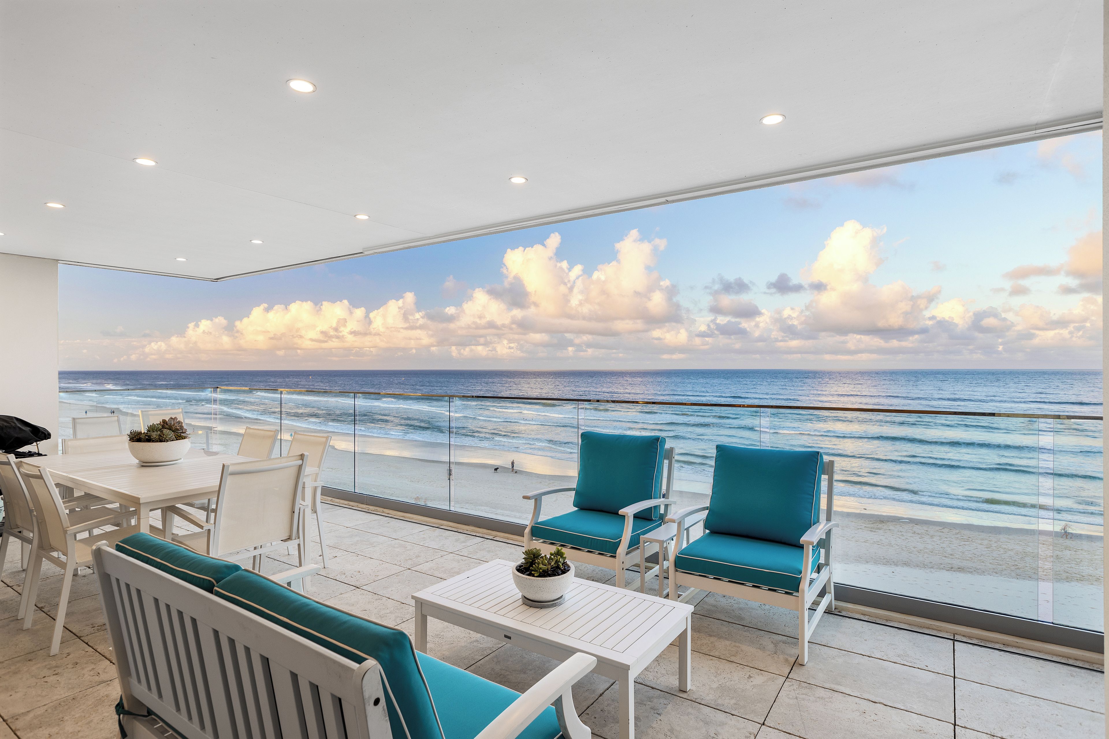 Un balcon avec vue sur l’océan, des meubles blancs et un plafond doté d’un éclairage encastré.