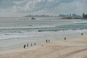 A beach with people walking and surfing, a distant city skyline, and a rocky outcrop. - Joy on Jefferson Stunning Palm Beach Escape (Palm Beach)