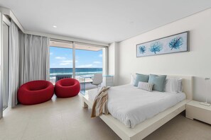 A modern hotel room with a large bed, a view of the sea, and a balcony with red chairs. - Joy on Jefferson Stunning Palm Beach Escape (Palm Beach)