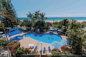 A pool area with multiple pools, lounge chairs, and umbrellas, surrounded by palm trees and overlooking a beach. - The Rocks Resort 3D Currumbin Ocean Views (Currumbin)