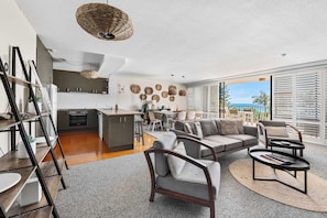 A modern living room with a sofa, coffee table, and a view of the ocean through large windows. - The Rocks Resort 3D Currumbin Ocean Views (Currumbin)