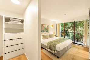 A bedroom with a bed, a nightstand, a painting, and a view of greenery through a window. - The Rocks Resort 4C Currumbin Beachfront Apartment (Currumbin)