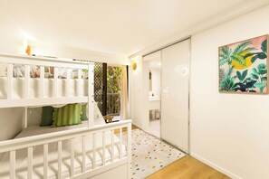 A room with a white crib, a colorful rug, and a tropical-themed painting on the wall. - The Rocks Resort 4C Currumbin Beachfront Apartment (Currumbin)