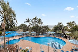 A swimming pool with lounge chairs and umbrellas, surrounded by palm trees. - The Rocks Resort 4C Currumbin Beachfront Apartment (Currumbin)