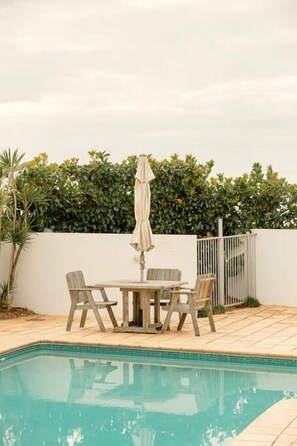 A swimming pool with a wooden deck, a table with chairs, and an umbrella. - Waves 203 on Currumbin Beach (Currumbin)