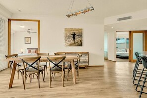 Une pièce spacieuse avec une table et des chaises en bois, un ventilateur de plafond et un tableau accroché au mur.