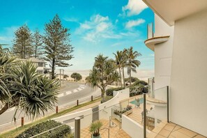 Ein Balkon mit Blick auf eine Straße, Palmen, einen Pool und ein modernes Gebäude.