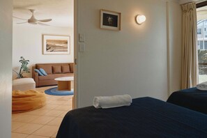A hotel room with a bed, a sofa, a small round table, a ceiling fan, and a framed picture on the wall. - Golden Era - Tugun Beachfront (Tugun)