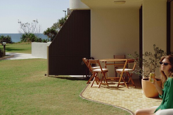 An outdoor seating area with a table and chairs, a potted plant, and a view of the sea. - Golden Era - Tugun Beachfront (Tugun)
