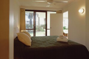 A hotel room with a bed, pillows, a ceiling fan, and a view of a palm tree and building through a glass door. - Golden Era - Tugun Beachfront (Tugun)