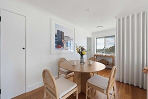 Un coin repas avec une table ronde en bois, quatre chaises, un vase de fleurs et un tableau encadré au mur.