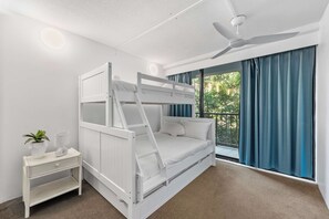 Una cama litera con escalera, una mesita de noche con lámpara y una ventana con cortinas.