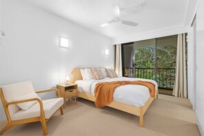 A bedroom with a bed, a chair, a nightstand, a ceiling fan, and a window with a view of greenery. - The Rocks Resort 2C Currumbin Beachfront (Currumbin)