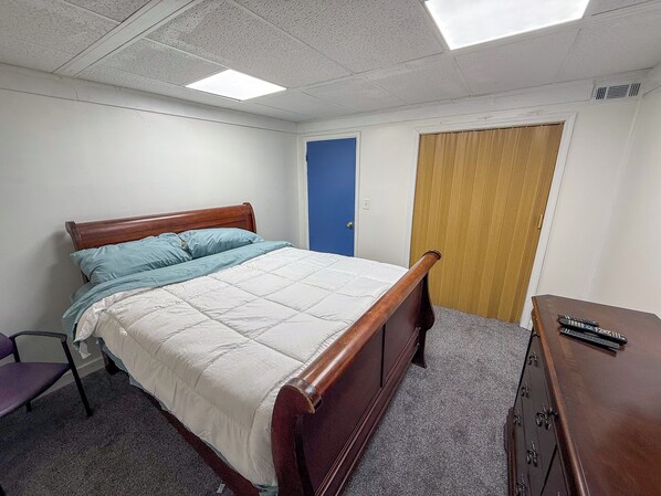 A bedroom with a bed, a chair, a dresser, and a door. - The Business Class Suite (College Park)
