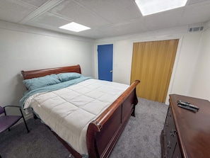 A bedroom with a bed, a chair, a dresser, and a door.